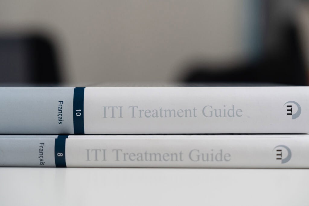 Two ITI Treatment Guide books stacked on a white surface, used by dental professionals for implantology procedures.
