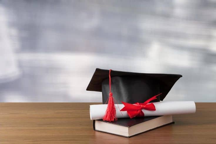 Graduation cap with red tassel and diploma on a book, symbolizing academic success and graduation achievement.