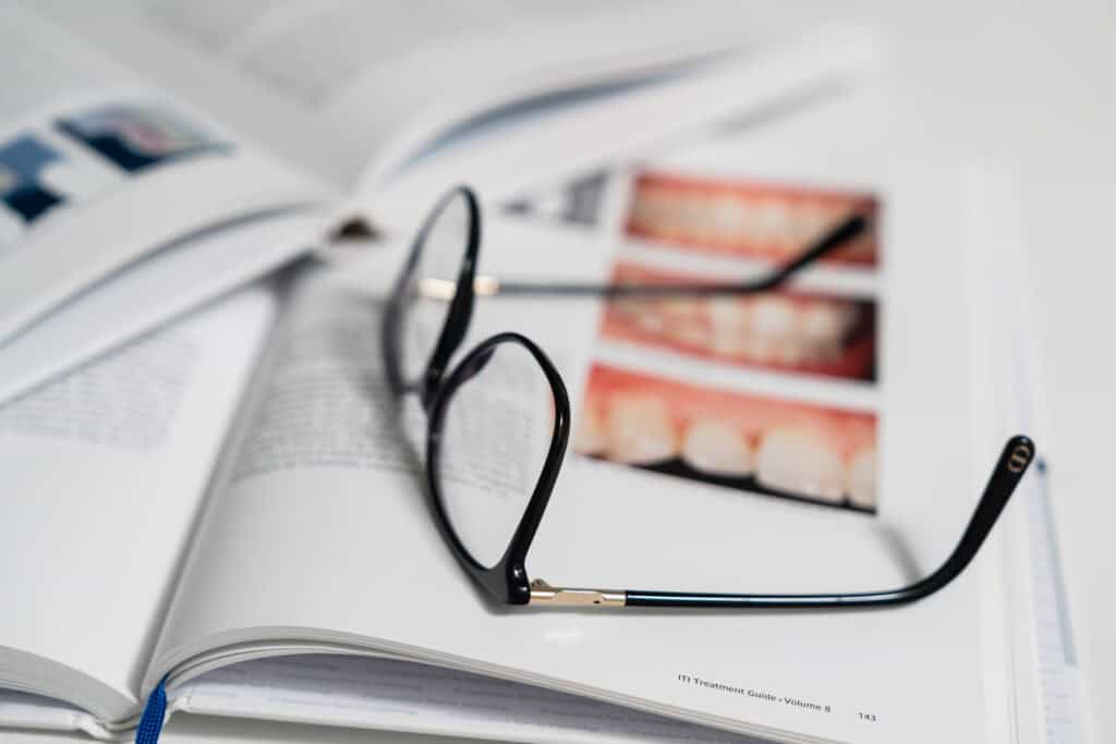 Lunettes posées sur un livre d’implantologie avec images cliniques